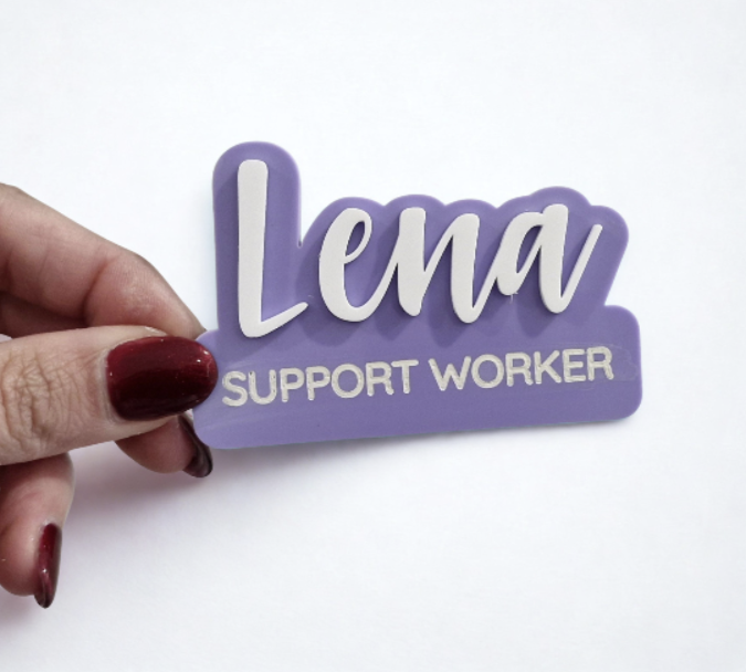 A hand with dark red nail polish holds a purple and white custom name sign that reads 'Lena SUPPORT WORKER' against a plain white background.