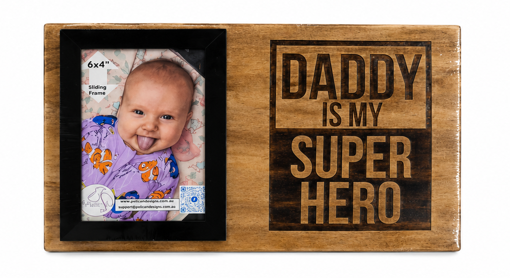 A wooden photo frame plaque with the engraved text 'DADDY IS MY SUPER HERO'. The top panel shows the front with a sample baby photo in the left slot and the text on the right.
