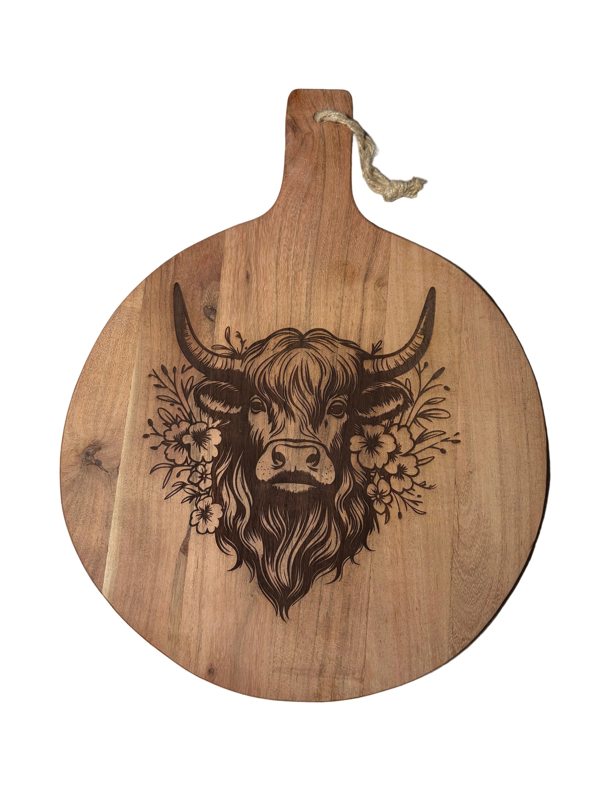 A round wooden serving board with a handle, featuring a dark engraved illustration of a highland cow head surrounded by flowers, with a small rope loop at the handle.