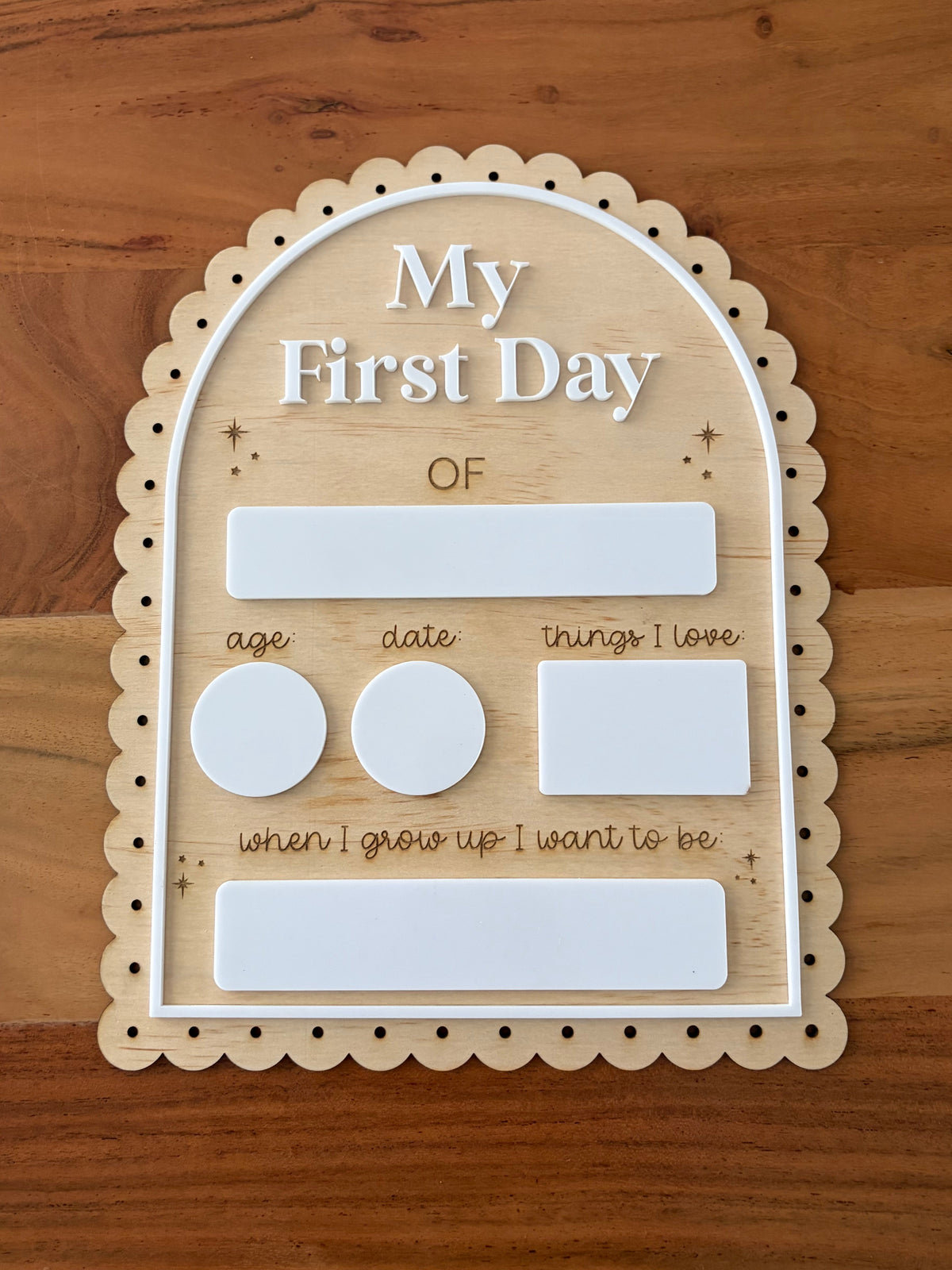 A wooden arch-shaped first-day-of-school-age milestone plaque with scalloped edges, featuring white labels for age, date, things I love, and a future goal, displayed on a wooden tabletop.