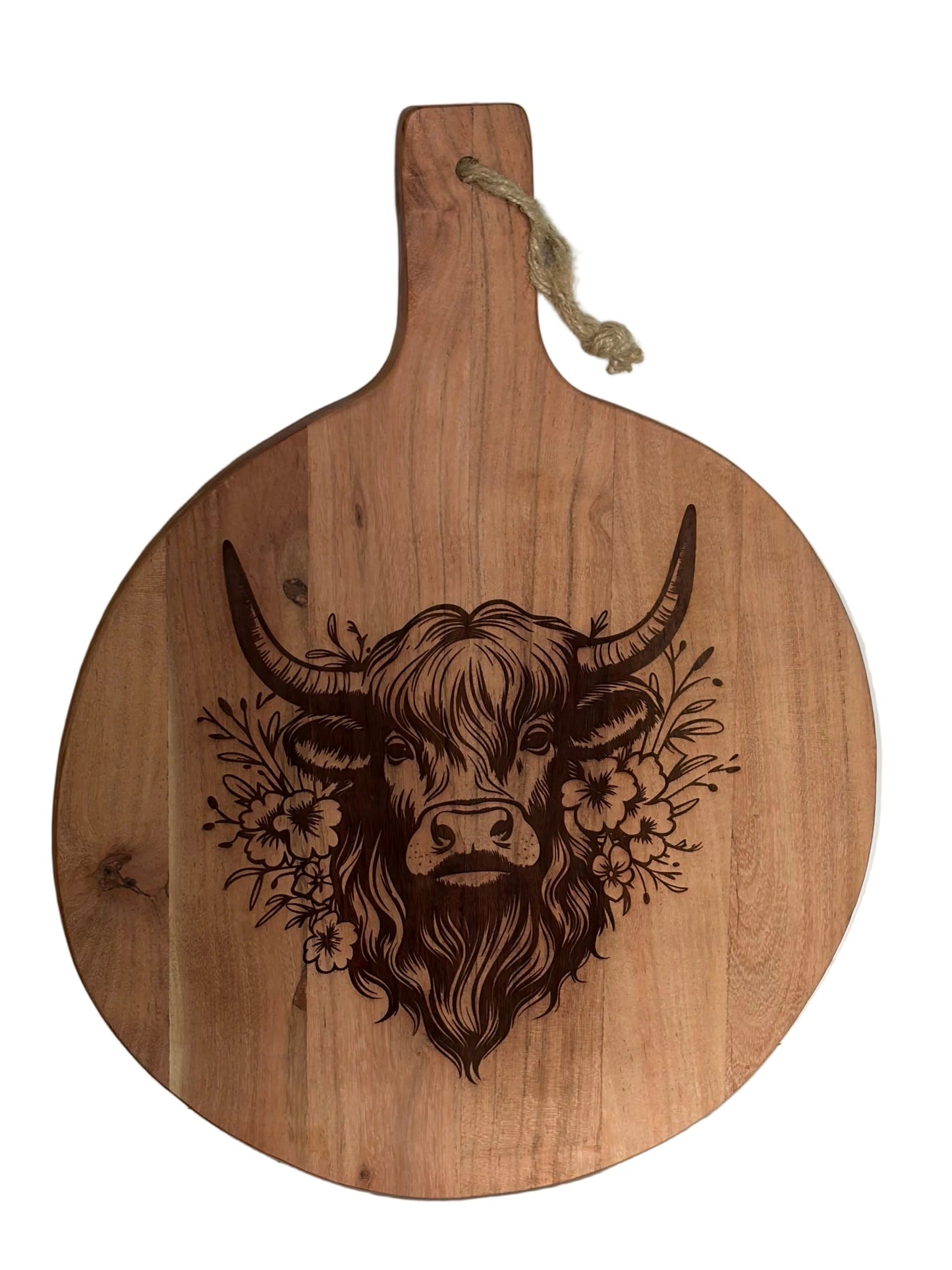 A round wooden serving board with a handle, featuring a dark brown engraved design of a highland cow surrounded by flowers.