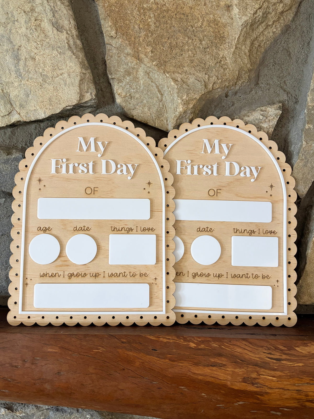 Two arched wooden photo plaques with scalloped edges, reading 'My First Day OF', displayed on a wooden surface in front of a stone wall. Each plaque has blank photo slots and small labeled fields for age, date, things I love, and a reflection for when I grew up.