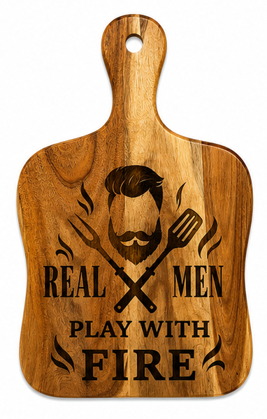 A wooden cutting board with a handle, featuring a laser-engraved graphic of a bearded man with crossed spatulas and the text 'REAL MEN PLAY WITH FIRE'.