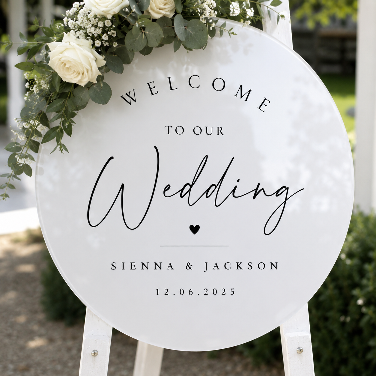 Personalised round acrylic wedding welcome sign displayed on a white easel with white roses, baby's breath and eucalyptus, custom made for weddings, birthdays and special events.