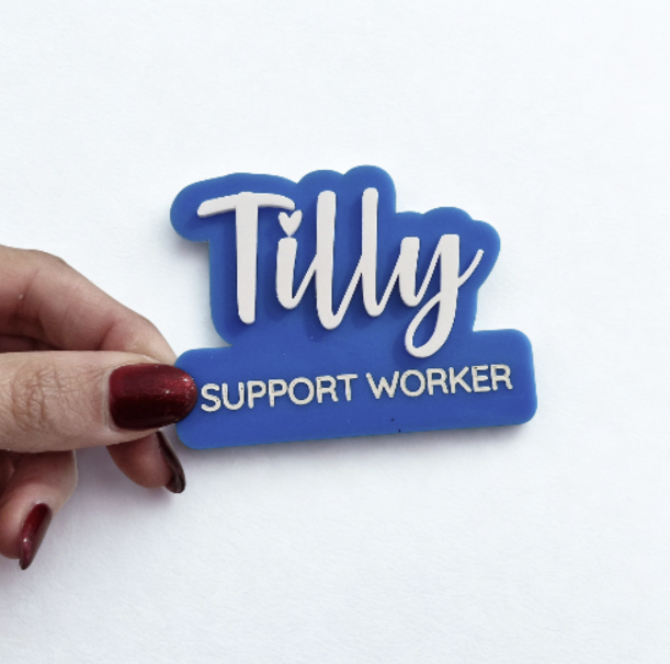 A hand with dark red nail polish holds a blue and white 'Tilly Support Worker' sign against a plain white background.