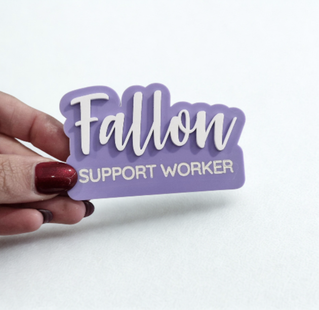 A hand with dark red nail polish holds a purple die-cut sticker that reads 'Fallon SUPPORT WORKER' in white lettering against a plain white background.