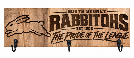 A rectangular wooden wall sign with three black hooks, featuring engraved text that reads 'SOUTH SYDNEY RABBITOHS EST 1906 THE PRIDE OF THE LEAGUE' alongside a rabbit outline, on a white background.